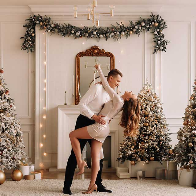 A couple elegantly dances in a festive room, surrounded by decorated Christmas trees. The mood is joyful and romantic, with warm, glowing lights.