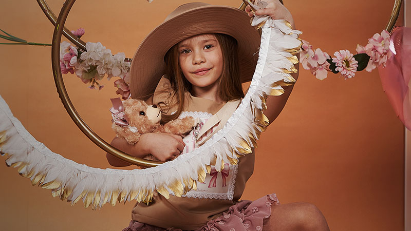 A girl in a hat holding a teddy bear 
