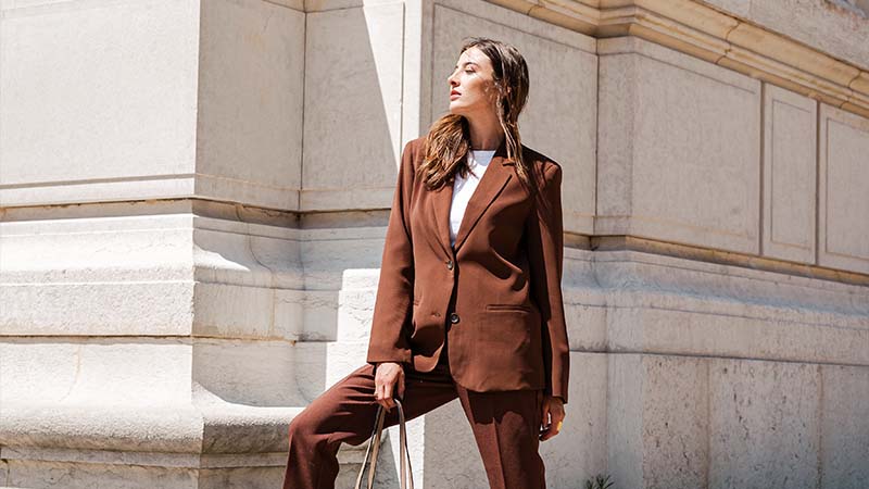 Woman in a brown pantsuit poses in front of the facade